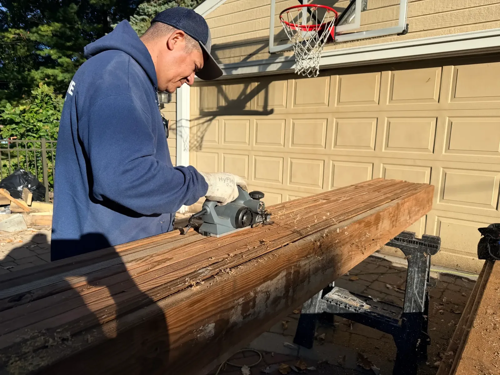 Carpenter using an electric planer to prepare lumber on sawhorses during the Evanston deck build