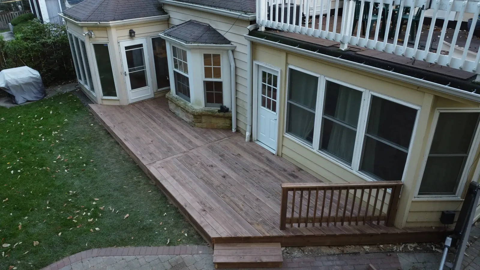 Low cedartone wood deck around a bay window, with a wood railing and step at an Evanston home