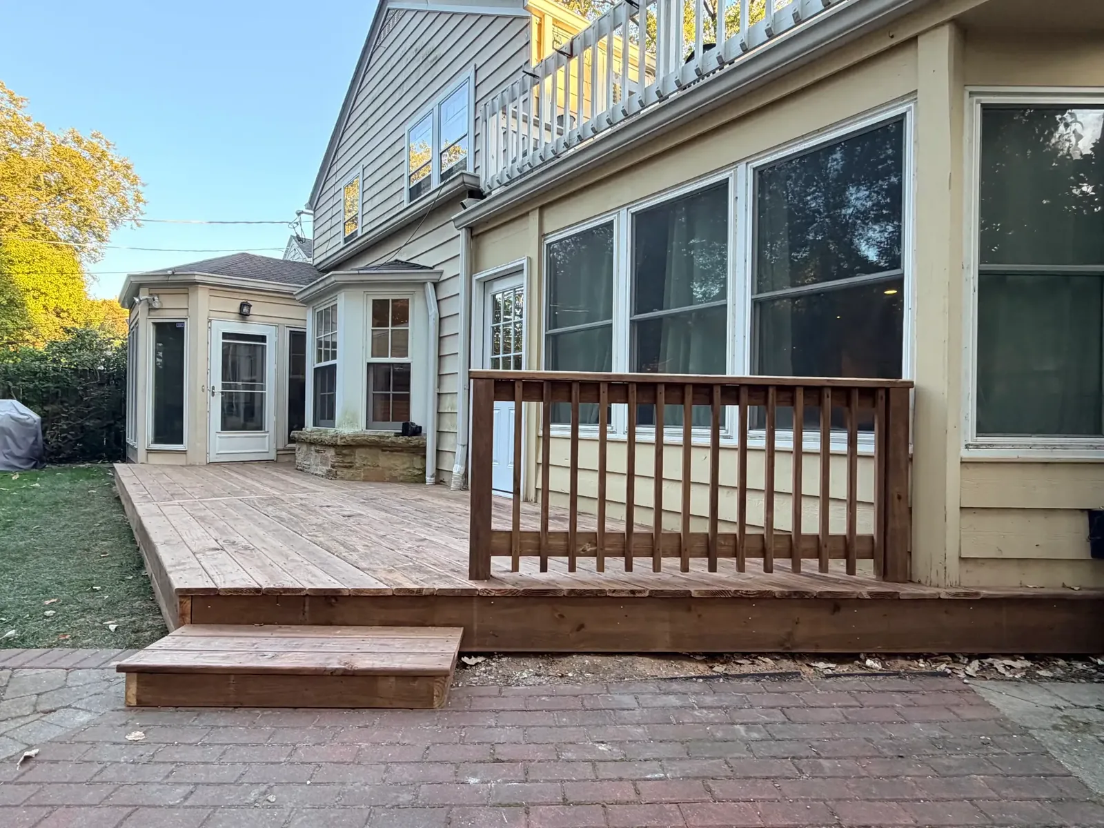 Wood railing with vertical balusters beside the deck step and paver patio