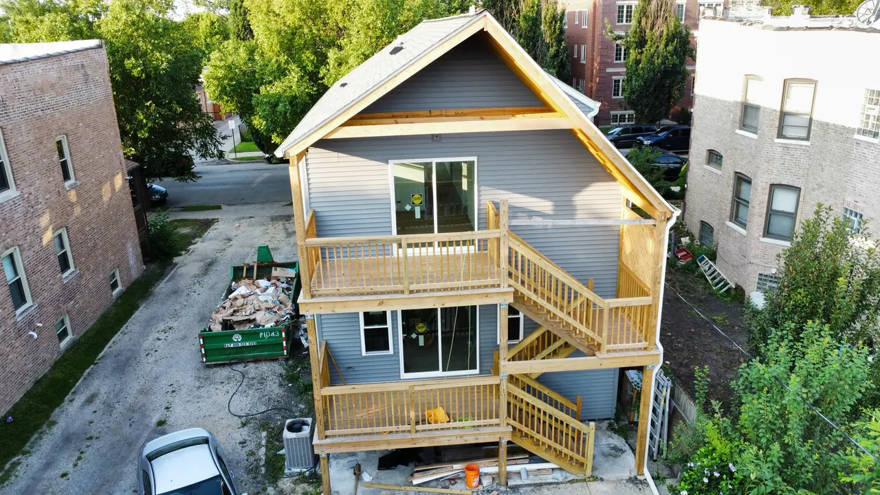 Construction-stage view of a multi-level wood rear porch with two stair runs, landings, railings, and a covered upper level